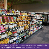 Picture of an aisle within PrairieLand Market featuring a number of packaged and canned goods. Text at the bottom of the image reads: More national brands are on their shelves because of belonging to the Independent Natural Food Retailers Association.