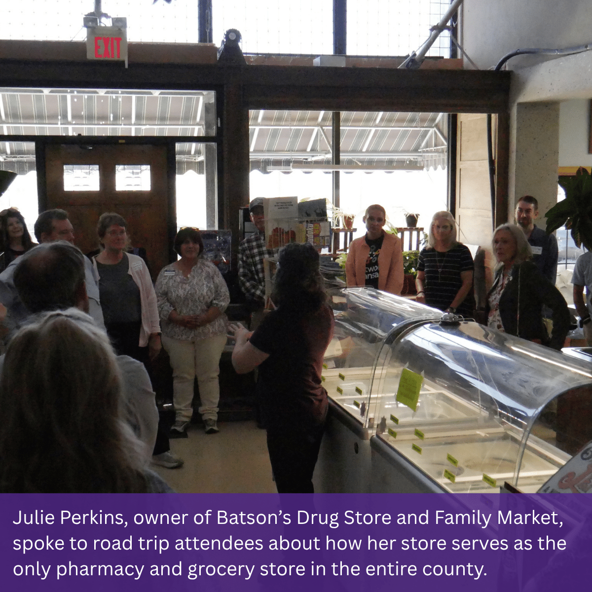 An individual standing in front of an ice cream case speaks to a group of road trip attendees.