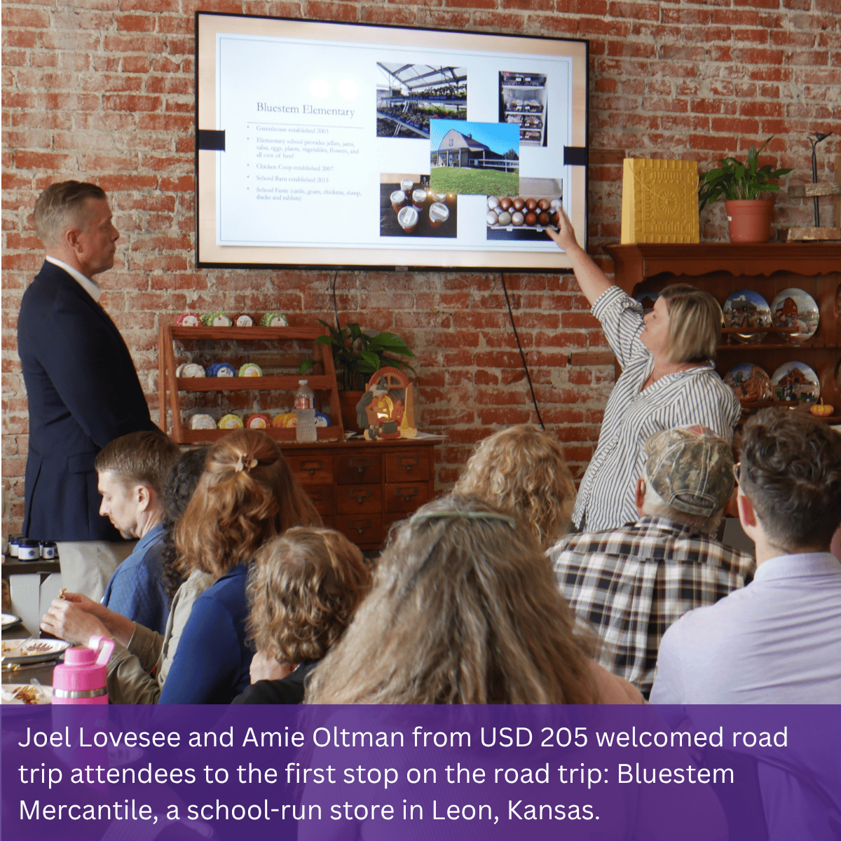 Two individuals presenting in a store with a screen behind them showing a slide with pictures while seven individuals seated at tables look at the screen.